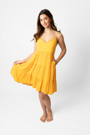 Brunette model facing front, wearing Yellow Mango Miami Tiered Strappy Mini Dress. Features adjustable straps, a flirty tiered empire silhouette, smocked back, and pockets. Crafted from lightweight rayon and lined in white. Perfect for date night or any vacation-ready occasion. Koy Resort affordable vacation, cruise, and resort-wear.