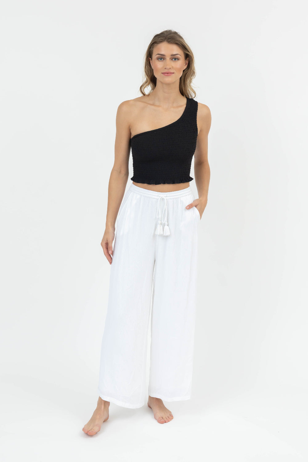 Woman wearing a black one-shoulder top and white pants on a white background