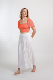 Blonde model facing front, wearing Orange Coral Punch Miami Boho Smocked Crop Top. Features a lightweight crinkle rayon fabric, flattering smocked detailing, flowy sleeves, and a cropped fit. Ideal for adding a boho chic touch to your summer wardrobe, perfect for travel and various occasions. Koy Resort affordable vacation, cruise, and resort-wear.