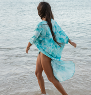 woman on the beach freely looking into the ocean wearing a flowy blue tie dye printed beach kimono