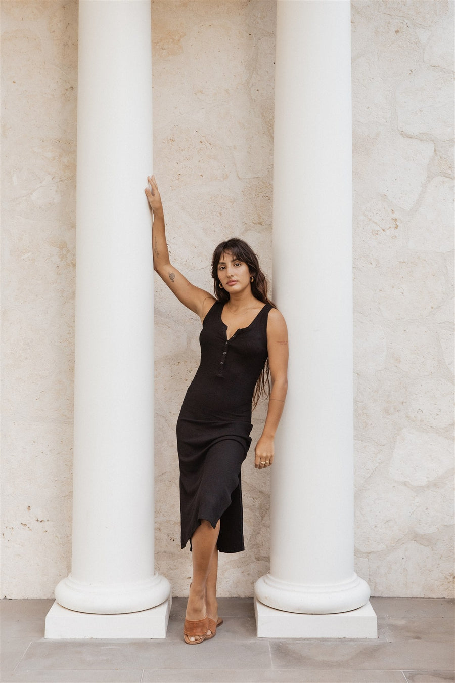 Brunette model facing front, wearing Black Laguna Rib Henley Midi Dress with ribbed cotton fabric, tonal buttons, v-neck, and side slit. Minimalistic design for effortless elegance and added comfort. Koy Resort affordable vacation, cruise, and resort-wear.