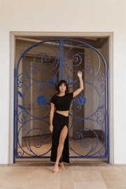 Brunette model facing front, wearing Black Laguna Rib Knot Top Maxi Skirt with ribbed cotton fabric, high dramatic slit, and knot top. Perfect for beach-to-street style and mix-and-match outfits. Koy Resort affordable vacation, cruise, and resort-wear.