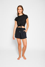 Brunette model facing front, wearing Black Miami Tie Front Shorts made from light crinkle rayon, featuring an adjustable elastic waistband with drawcord, pockets, and lining in white. Perfect for an everyday casual look. Koy Resort affordable vacation, cruise, and resort-wear.