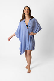 Brunette model facing front, wearing Bahama Blue Miami Big Shirt Button Up Dress. Features a structured collar, delicate button details, short sleeves, and flowy slits. Oversized and flowy with an asymmetrical hem, side slit, and back yoke. Perfect for breezy beach days. Koy Resort affordable vacation, cruise, and resort-wear.