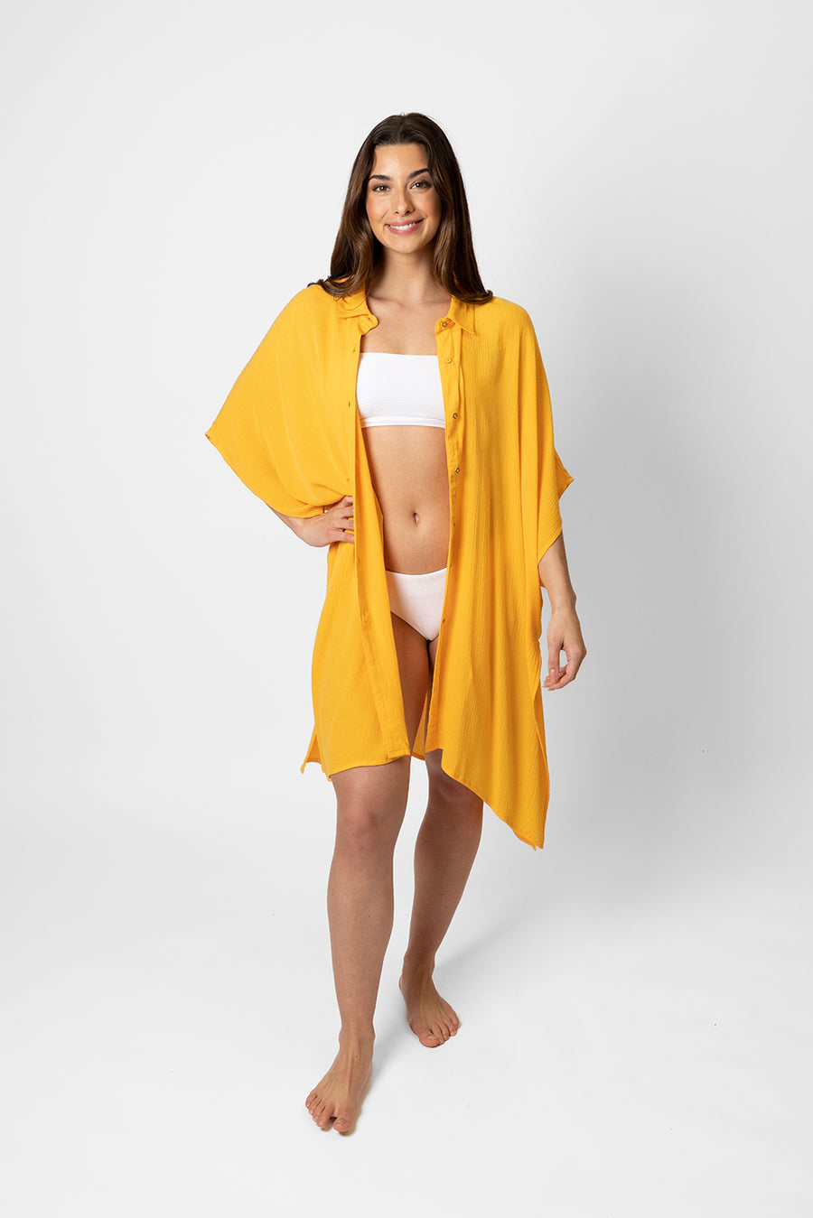 Brunette model facing front, wearing Yellow Mango Miami Big Shirt Button Up Dress. Features a structured collar, delicate button details, short sleeves, and flowy slits. Oversized and flowy with an asymmetrical hem, side slit, and back yoke. Perfect for breezy beach days. Koy Resort affordable vacation, cruise, and resort-wear.