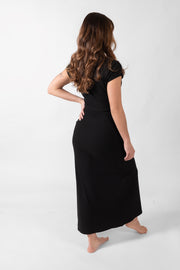 Brunette model facing back, wearing Black Laguna Rib Twisted Crop Top with short sleeves, ribbed fabric, twist hem, and crew neck. Flattering and chic for beach-to-street transitions. Perfect for pairing with the Laguna Rib Mini Skirt or Knot Maxi Skirt. Koy Resort affordable vacation, cruise, and resort-wear.