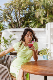 Brunette model facing front close up, wearing the Margarita Green Laguna Rib Twisted Crop Top. The top features short sleeves, rib fabric, a twist hem, and a crew neck, offering a chic and flattering fit. Made from 92% Rayon and 8% Spandex. Available in black or striking lime margarita. Koy Resort affordable vacation, cruise, and resort-wear.