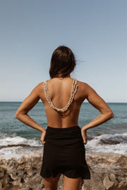 Brunette model facing back close up, wearing Black Laguna Rib Twisted Knot Top Mini Skirt with chic ribbed fabric, figure-flattering fit, knot top, side slit, and elastic back. Perfect for mix and match style and comfort. Koy Resort affordable vacation, cruise, and resort-wear.