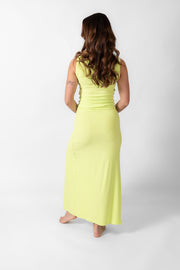 Brunette model facing back, wearing the Margarita Green Laguna Rib Knot Top Maxi Skirt. This skirt features a ribbed finish, high dramatic slit, and a knot top design. Made from 92% Rayon and 8% Spandex, it's perfect for beach-to-street style. Koy Resort affordable vacation, cruise, and resort-wear.