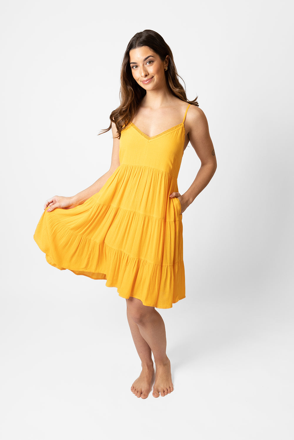 Brunette model facing front, wearing Yellow Mango Miami Tiered Strappy Mini Dress. Features adjustable straps, a flirty tiered empire silhouette, smocked back, and pockets. Crafted from lightweight rayon and lined in white. Perfect for date night or any vacation-ready occasion. Koy Resort affordable vacation, cruise, and resort-wear.