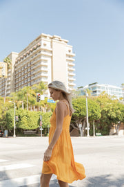 Blonde model facing side, wearing Yellow Mango Miami Tiered Strappy Mini Dress. Features adjustable straps, a flirty tiered empire silhouette, smocked back, and pockets. Crafted from lightweight rayon and lined in white. Perfect for date night or any vacation-ready occasion. Koy Resort affordable vacation, cruise, and resort-wear.