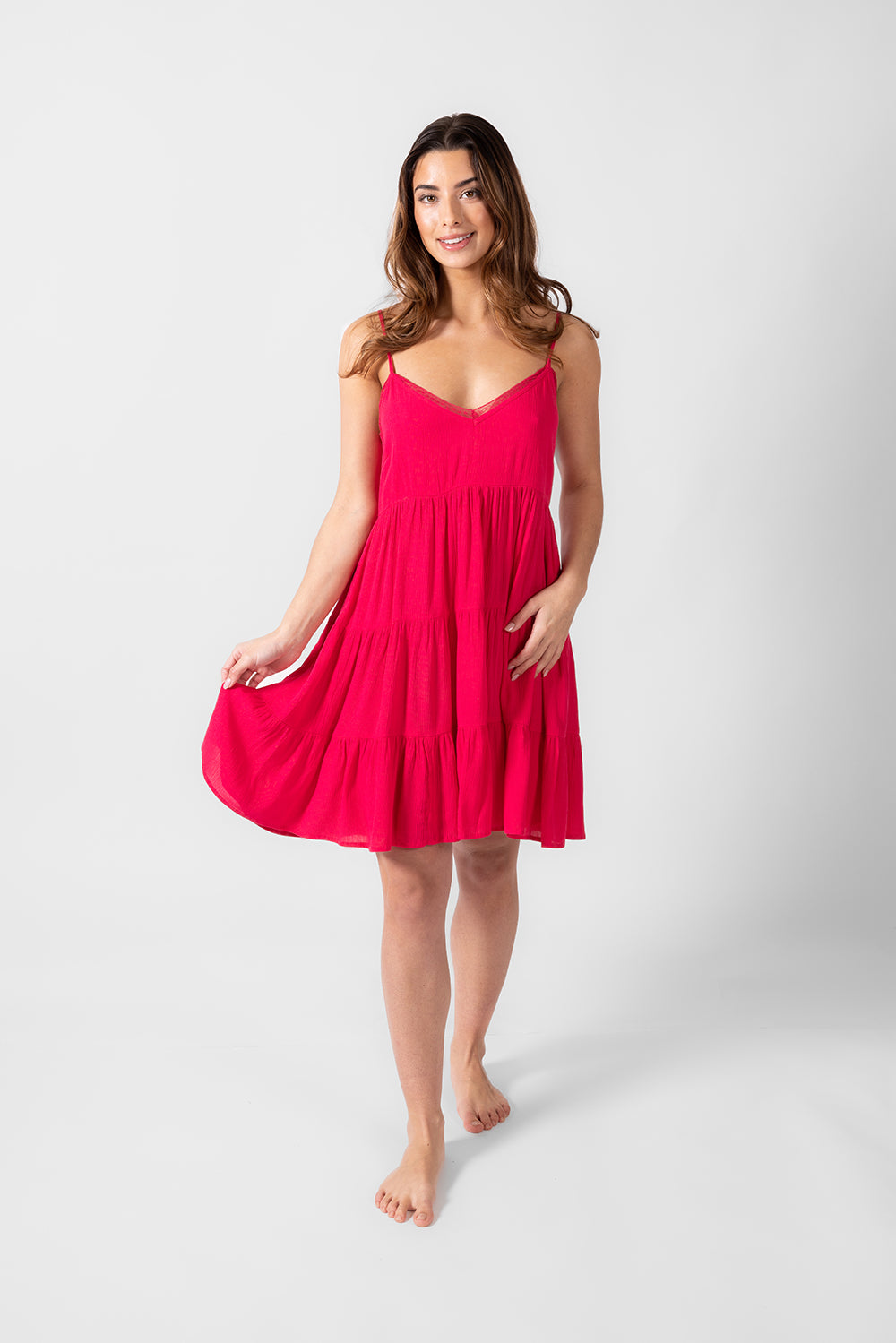 a front shot of a brunette hair woman holding the edge of her raspberry colored spaghetti strap summer beach dress