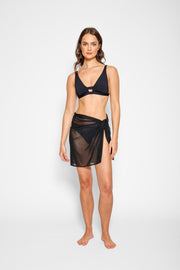 Brunette model facing front, wearing the Black Escape Mesh Mini Sarong Skirt. This versatile mini sarong is crafted from exclusive mesh fabric, ideal for beach or pool days. The semi-sheer design offers a trendy, effortless look, with multiple tying options for a personalized style. Koy Resort affordable vacation, cruise, and resort-wear.