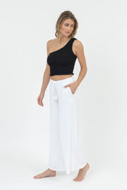Woman wearing a black one-shoulder top and white pants on a white background