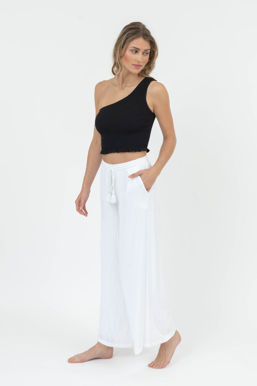 Woman wearing a black one-shoulder top and white pants on a white background