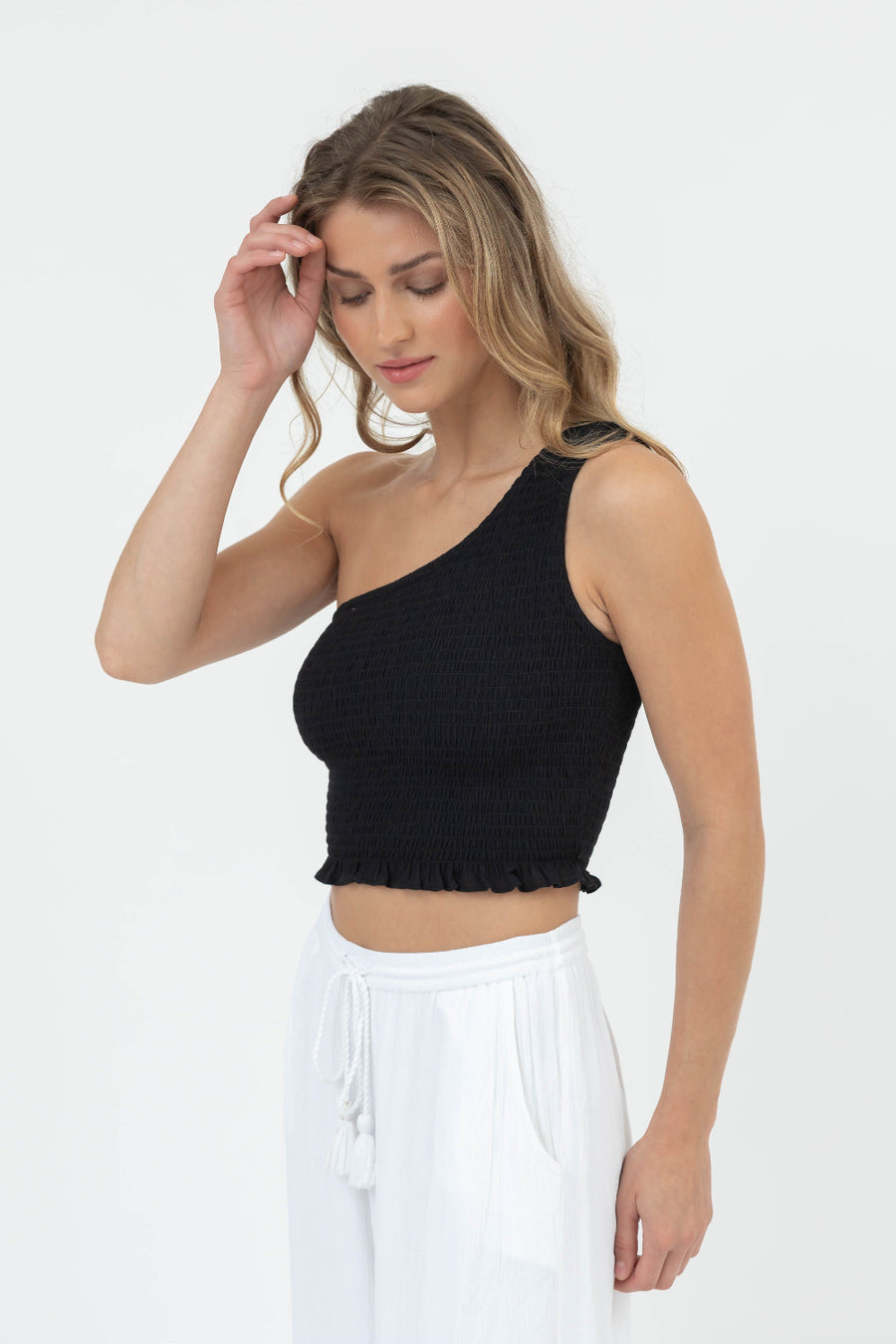Woman wearing a black one-shoulder top and white pants on a white background