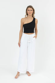 Woman wearing a black one-shoulder top and white pants on a white background