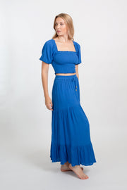 Blonde model facing side, wearing Blue Cobalt Miami Boho Smocked Crop Top. Features a lightweight crinkle rayon fabric, flattering smocked detailing, flowy sleeves, and a cropped fit. Ideal for adding a boho chic touch to your summer wardrobe, perfect for travel and various occasions. Koy Resort affordable vacation, cruise, and resort-wear.