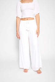 Brunette model facing front close up, wearing White Miami Wide Leg Pant with a tie waist, palazzo style, flowy straight leg, elastic waist, side pockets, and metallic tassel drawcord. Koy Resort affordable vacation, cruise, and resort-wear.