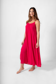 A brunette hair model having a side shot wearing a raspberry color strappy side split midi dress. Brunette model facing front, wearing Raspberry Pink Miami Side Slit Strappy Midi Dress. The dress features a strappy silhouette, midi length, and breezy material, with side slits and an adjustable cord at the back. The dress is lined in white, offering a loose and flowy fit perfect for effortless, fashion-forward looks. Koy Resort affordable vacation, cruise, and resort-wear.