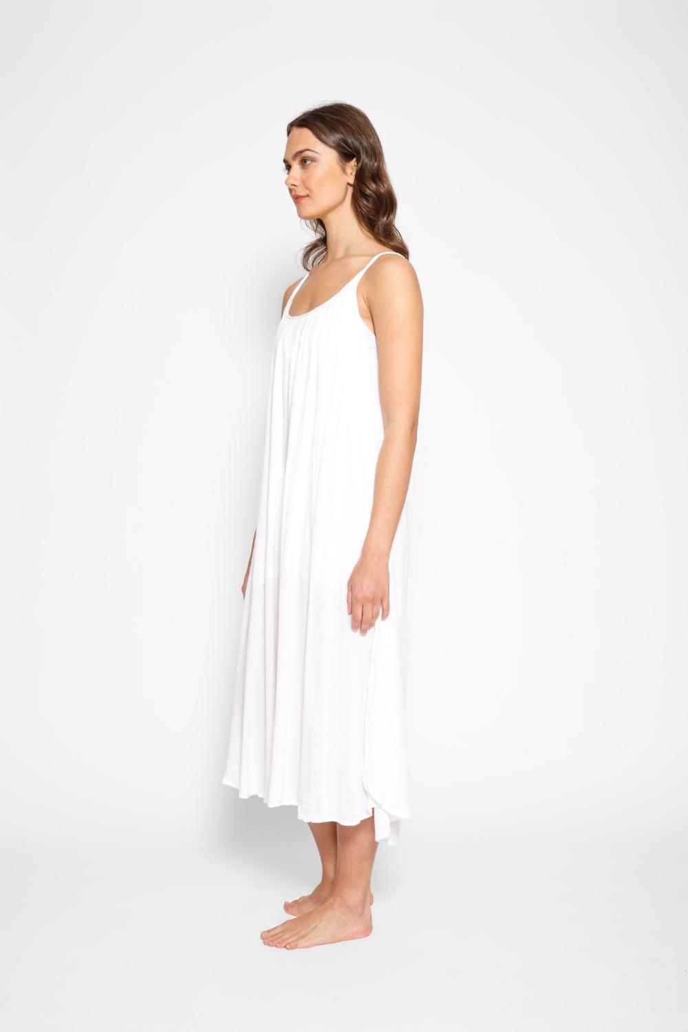 Brunette model facing side, wearing White Miami Side Slit Strappy Midi Dress with a loose and flowy fit, side slits, white lining, and adjustable cord at the back. Made from breezy rayon fabric for an effortless and fashion-forward look. Koy Resort affordable vacation, cruise, and resort-wear.