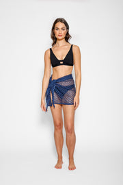 Brunette model facing front, wearing Navy Zuma Sheer Crochet Mini Sarong Skirt with herringbone zigzag crochet, adjustable tie style, side slit, and sheer fabric. Koy Resort affordable vacation, cruise, and resort-wear.