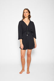 Brunette model facing front, wearing Black Miami Cinched Front Dress with butterfly sleeves, ruched center front with a tassel pull detail, adjustable straps, and side slits. Koy Resort affordable vacation, cruise, and resort-wear.