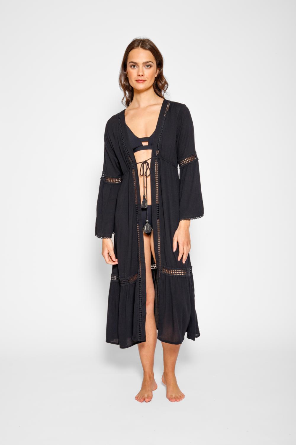 Brunette model facing front, wearing Black Miami Luxe Long Sleeve Robe with bell sleeves, maxi length, and tie front. Features crochet detailing, luxury lace trim, and pockets. Made of 100% crinkle rayon. Perfect for a sophisticated and comfortable look. Koy Resort affordable vacation, cruise, and resort-wear.