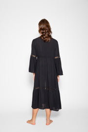 Brunette model facing back, wearing Black Miami Luxe Long Sleeve Robe with bell sleeves, maxi length, and tie front. Features crochet detailing, luxury lace trim, and pockets. Made of 100% crinkle rayon. Perfect for a sophisticated and comfortable look. Koy Resort affordable vacation, cruise, and resort-wear.