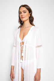 Brunette model facing front close up, wearing White Miami Luxe Long Sleeve Robe with bell sleeves, maxi length, and tie front. Features crochet detailing, luxury lace trim, and pockets. Made of 100% crinkle rayon. Perfect for a sophisticated and comfortable look. Koy Resort affordable vacation, cruise, and resort-wear.