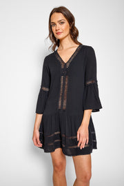 Brunette model facing front close up, wearing Black Miami Luxe Drop Waist Dress with luxury lace trim, drop waist, v-neck, and flutter sleeves. Fun and flirty short dress perfect for any occasion. Koy Resort affordable vacation, cruise, and resort-wear.