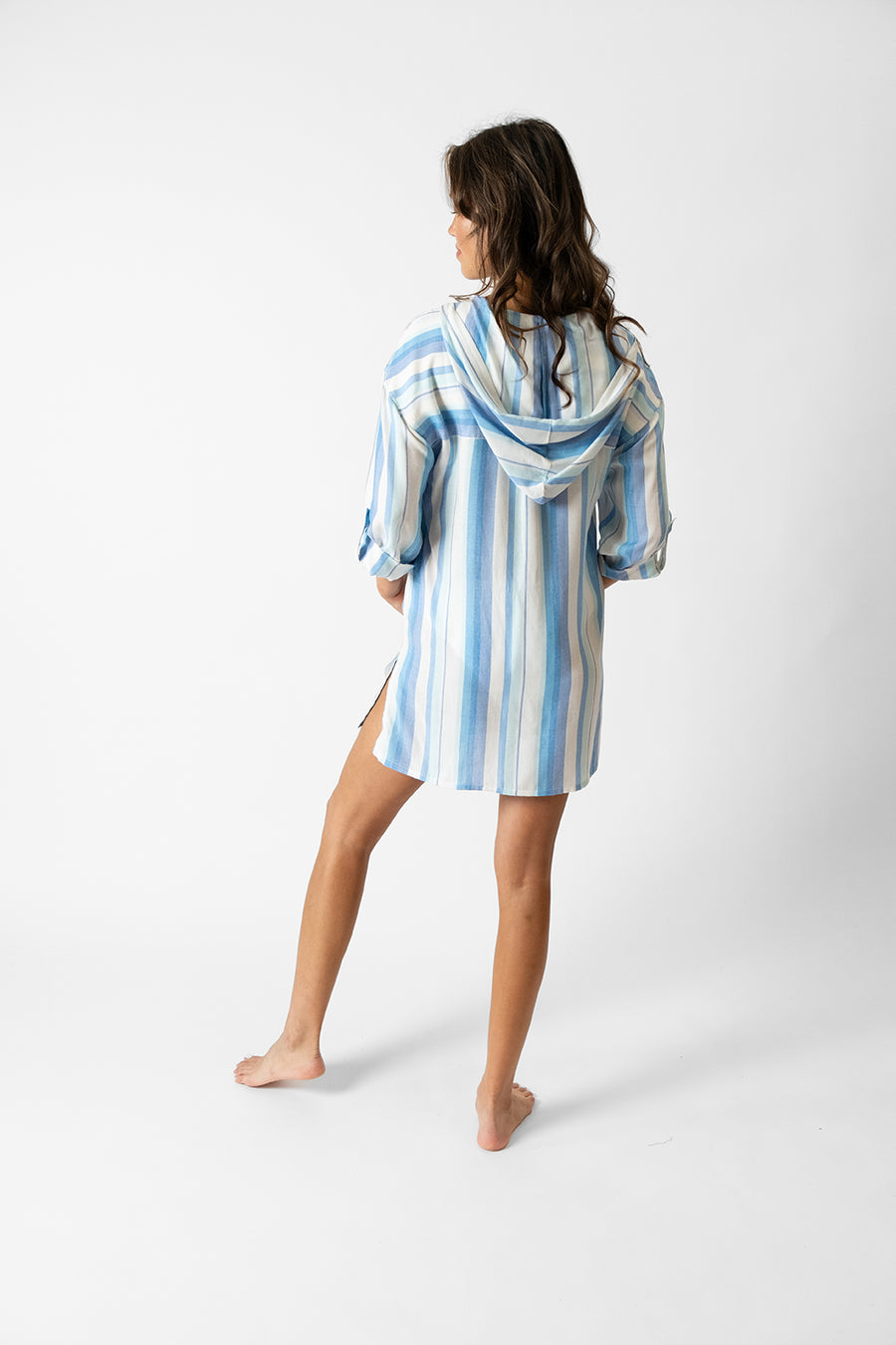 Brunette model facing back, wearing Taormina Blue Sicily Hooded Cover Up with a lace-up neckline, hood, kangaroo pocket, mini length, and rolled-up sleeves. Koy Resort affordable vacation, cruise, and resort-wear.