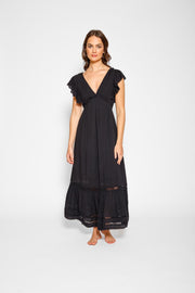 Brunette model facing front, wearing Black Miami Luxe Ruffle Sleeve Maxi Dress with ruffle sleeves, deep v-neck, semi-exposed back, empire waist, luxury crochet details, and frill hem. Koy Resort affordable vacation, cruise, and resort-wear.