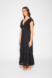 Brunette model facing side, wearing Black Miami Luxe Ruffle Sleeve Maxi Dress with ruffle sleeves, deep v-neck, semi-exposed back, empire waist, luxury crochet details, and frill hem. Koy Resort affordable vacation, cruise, and resort-wear.