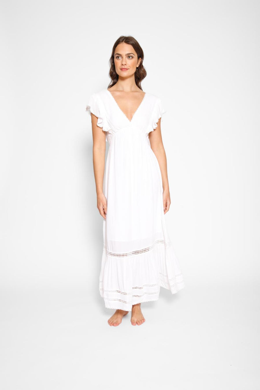 Brunette model facing front, wearing White Miami Luxe Ruffle Sleeve Maxi Dress with ruffle sleeves, deep v-neck, semi-exposed back, empire waist, luxury crochet details, and frill hem. Koy Resort affordable vacation, cruise, and resort-wear.