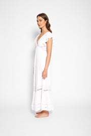 Brunette model facing side, wearing White Miami Luxe Ruffle Sleeve Maxi Dress with ruffle sleeves, deep v-neck, semi-exposed back, empire waist, luxury crochet details, and frill hem. Koy Resort affordable vacation, cruise, and resort-wear.