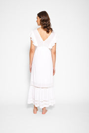 Brunette model facing back, wearing White Miami Luxe Ruffle Sleeve Maxi Dress with ruffle sleeves, deep v-neck, semi-exposed back, empire waist, luxury crochet details, and frill hem. Koy Resort affordable vacation, cruise, and resort-wear.