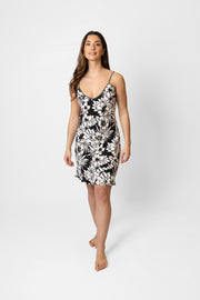 Brunette model facing front, wearing Black Onyx Copacabana Floral Strappy Mini Cami Dress. This dress features a tropical hibiscus print, adjustable spaghetti straps, and a v-neck. Made from 100% sand-washed rayon, it offers a cool and comfortable fit, ideal for parties or casual outings. Koy Resort affordable vacation, cruise, and resort-wear.