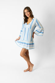 Brunette model facing front, wearing Taormina Blue Sicily Tunic with a flirty v-neck, bell 3/4 sleeves, side pockets, frill sleeves, flared hem, and mini length. Koy Resort affordable vacation, cruise, and resort-wear.