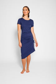 Brunette model facing front, wearing Navy Laguna Beach Midi Dress with adjustable side gathering, scoop neck, short sleeves, asymmetrical hem, and a figure-flattering fit. Made from a cozy cotton jersey blend for stylish and comfortable wear. Koy Resort affordable vacation, cruise, and resort-wear.