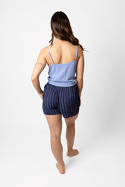 Brunette model facing back, wearing navy Marina Stripe Front Tie Shorts. Features include a blue mock stitch print, loose fit, and side pockets. Made from comfortable crinkle rayon fabric, perfect for vacation or everyday wear. Koy Resort affordable vacation, cruise, and resort-wear.