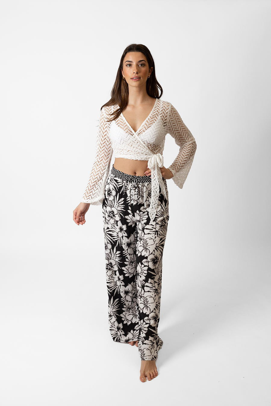 Brunette model facing front, wearing Black Onyx Copacabana Floral Wide Leg Pant. Features a vibrant hibiscus floral print, wide leg palazzo style, and an adjustable cinched waist with pockets. Crafted from 100% sand-washed rayon, perfect for a garden-chic look or vacation style. Koy Resort affordable vacation, cruise, and resort-wear.