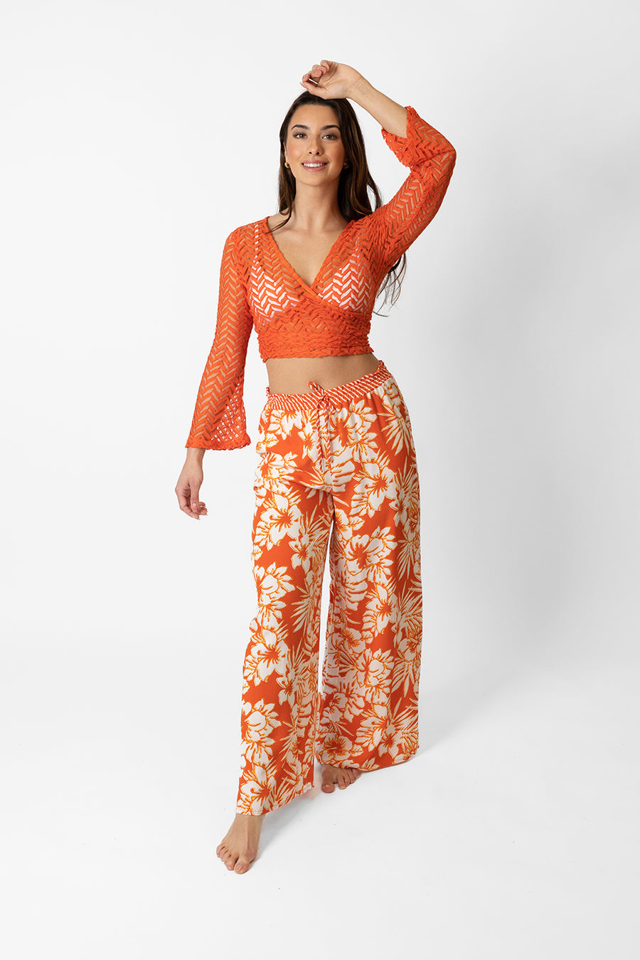 Brunette model facing front, wearing Orange Spritz Copacabana Floral Wide Leg Pant. Features a vibrant hibiscus floral print, wide leg palazzo style, and an adjustable cinched waist with pockets. Crafted from 100% sand-washed rayon, perfect for a garden-chic look or vacation style. Koy Resort affordable vacation, cruise, and resort-wear.