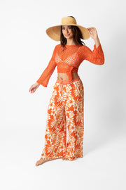 Brunette model facing side, wearing Orange Spritz Copacabana Floral Wide Leg Pant. Features a vibrant hibiscus floral print, wide leg palazzo style, and an adjustable cinched waist with pockets. Crafted from 100% sand-washed rayon, perfect for a garden-chic look or vacation style. Koy Resort affordable vacation, cruise, and resort-wear.