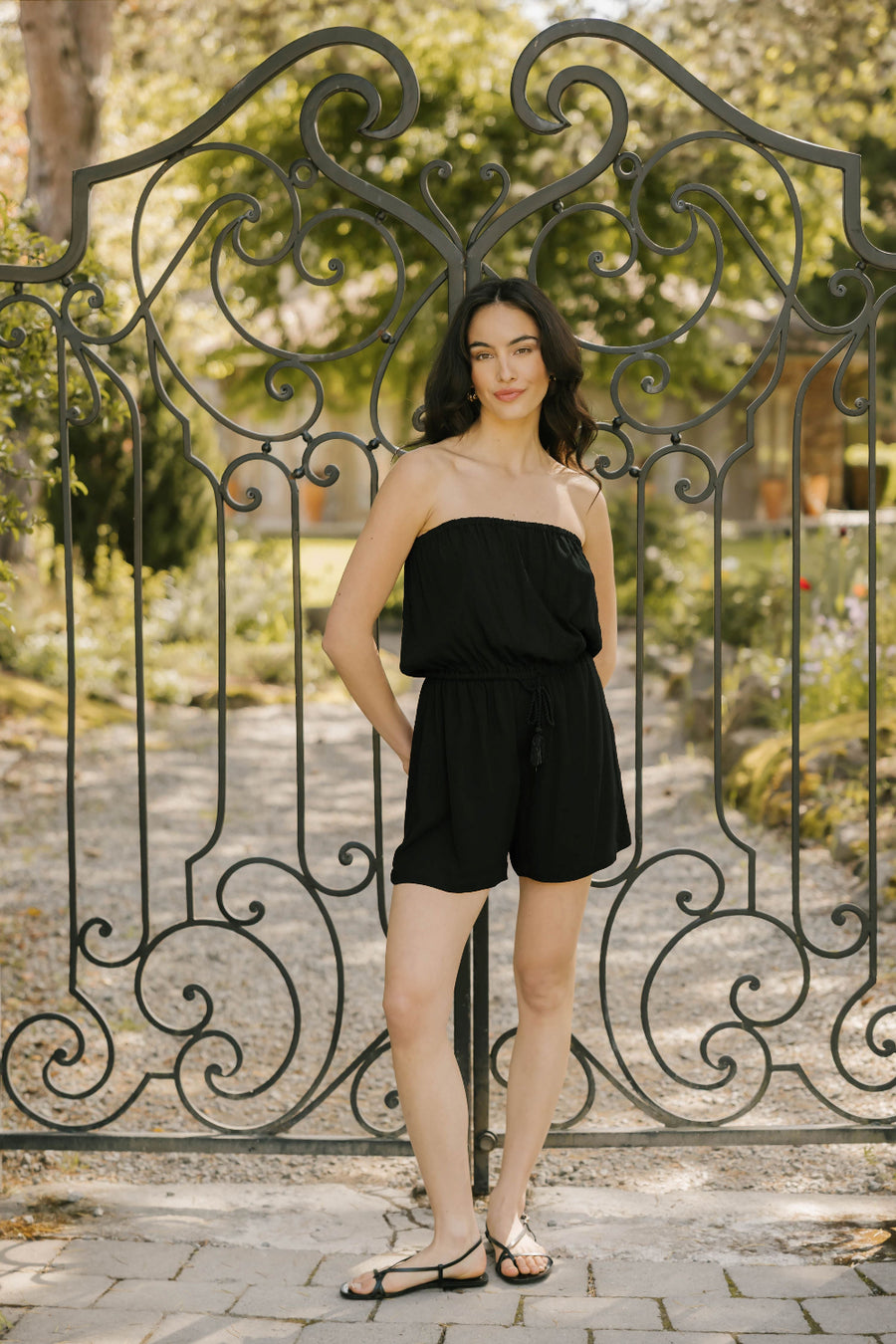 Woman in a black outfit standing in front of an ornate metal gate.