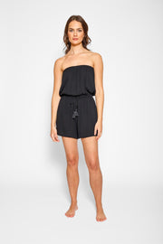 Brunette model facing front, wearing Black Miami Romper with an elastic top, adjustable waist with a tassel detail, elastic waist, and pockets. Koy Resort affordable vacation, cruise, and resort-wear