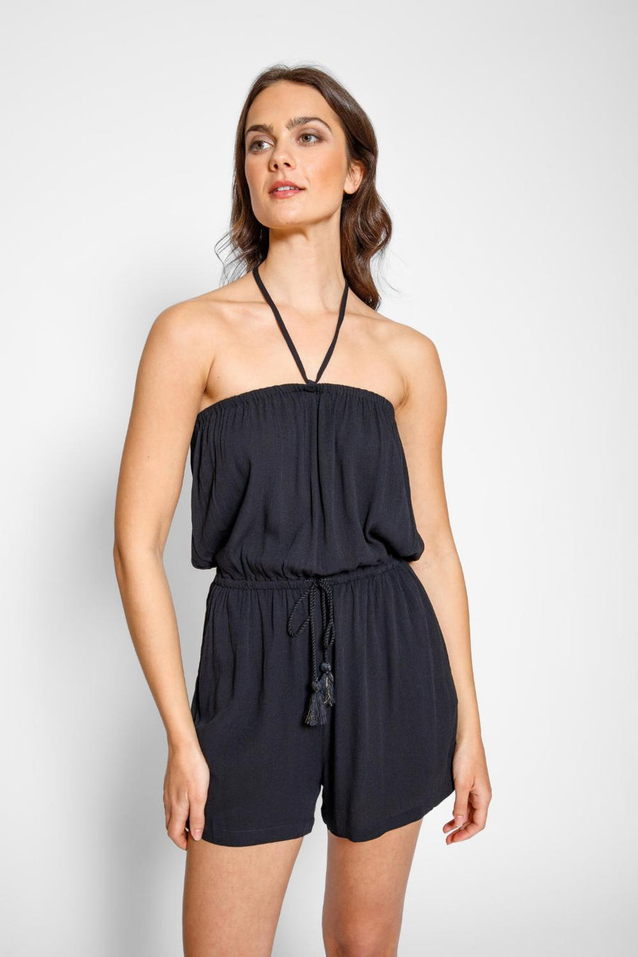 Brunette model facing front close up, wearing Black Miami Romper with an elastic top, adjustable waist with a tassel detail, elastic waist, and pockets. Koy Resort affordable vacation, cruise, and resort-wear