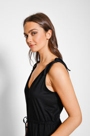 Brunette model facing side close up, wearing Black Laguna Beach Romper, made of soft jersey spandex fabric with adjustable straps and pockets. Koy Resort affordable vacation, cruise, and resort-wear