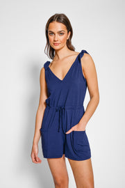 Brunette model facing front close up, wearing Navy Laguna Beach Romper, made of soft jersey spandex fabric with adjustable straps and pockets. Koy Resort affordable vacation, cruise, and resort-wear