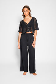 Brunette model facing front, wearing Black Miami Wide Leg Pant with a tie waist, palazzo style, flowy straight leg, elastic waist, side pockets, and metallic tassel drawcord. Koy Resort affordable vacation, cruise, and resort-wear.